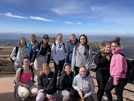 Gruppe von Schülerinnen mit Lehrkraft vor Bergpanorama in Barcelona
